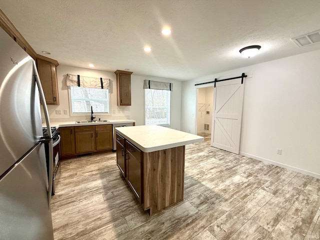 kitchen featuring a center island, sink, a barn door, a textured ceiling, and appliances with stainless steel finishes