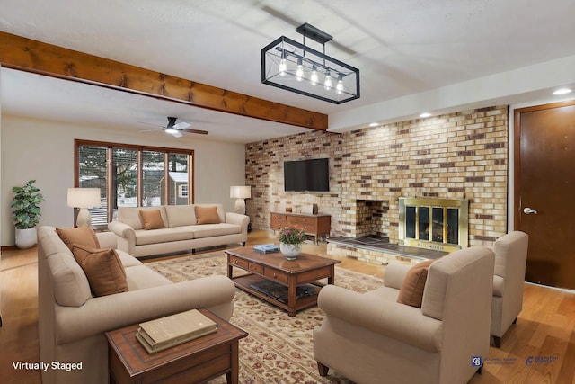 living room with ceiling fan, light hardwood / wood-style floors, a fireplace, beam ceiling, and brick wall