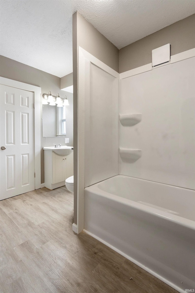 full bathroom featuring vanity, hardwood / wood-style floors, a textured ceiling, toilet, and shower / bathing tub combination