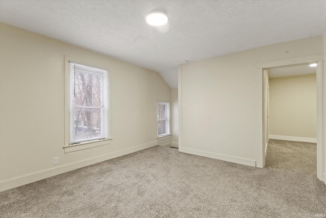 empty room with lofted ceiling, light carpet, and a textured ceiling