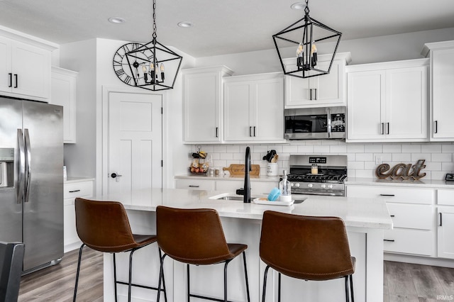 kitchen featuring a center island with sink, decorative light fixtures, white cabinetry, and appliances with stainless steel finishes