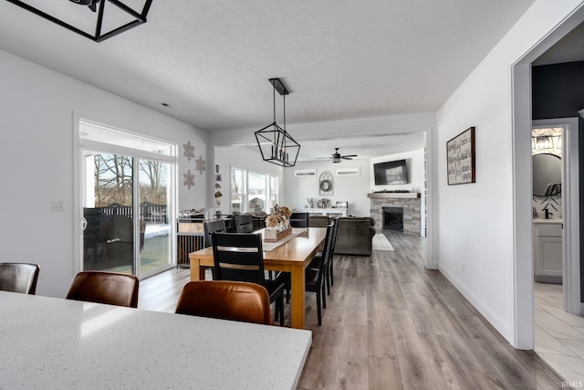 dining room featuring ceiling fan with notable chandelier, a stone fireplace, sink, light wood-type flooring, and a textured ceiling