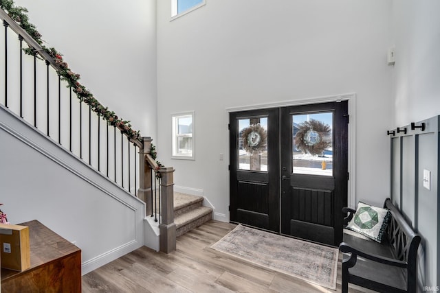 entryway featuring light hardwood / wood-style floors, a towering ceiling, and french doors