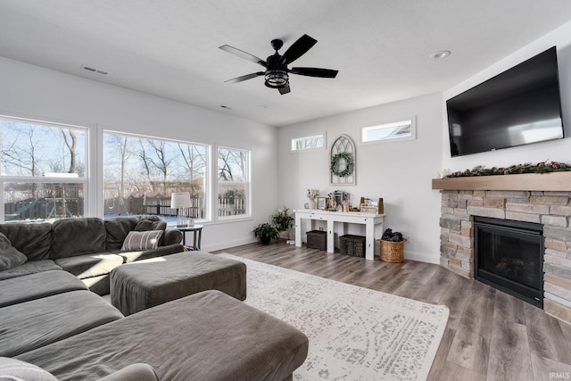 living room with hardwood / wood-style flooring, ceiling fan, and a stone fireplace