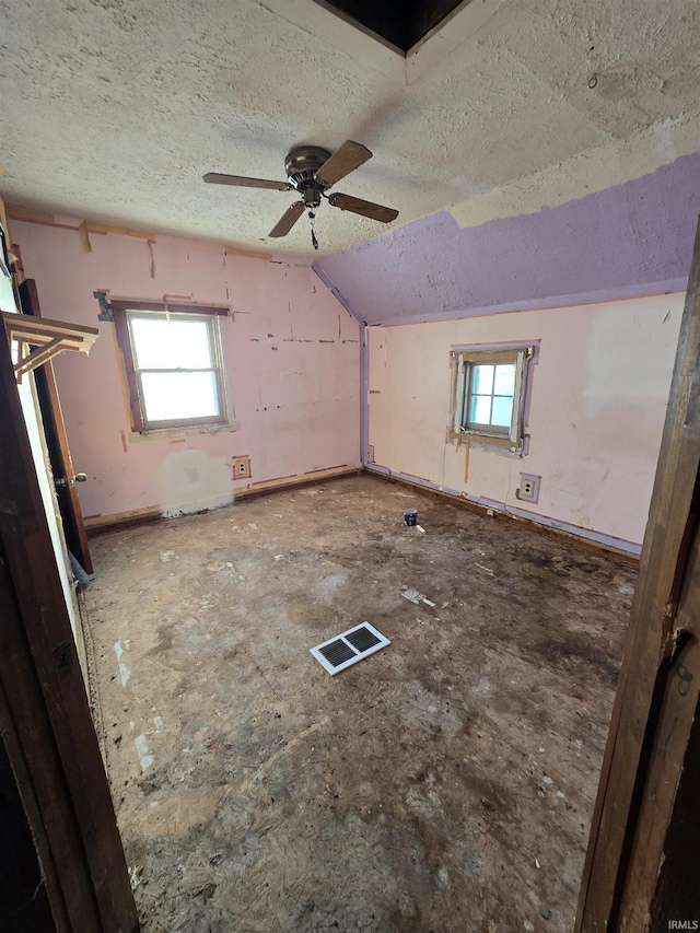 empty room with a wealth of natural light, a textured ceiling, ceiling fan, and lofted ceiling