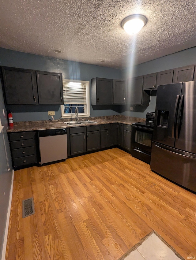 kitchen with light wood-type flooring, a textured ceiling, stainless steel appliances, and sink