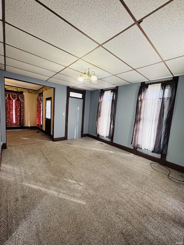 carpeted spare room featuring a paneled ceiling and an inviting chandelier