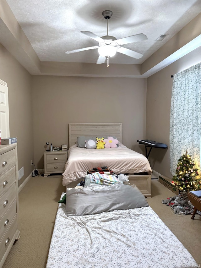 bedroom featuring a textured ceiling, light colored carpet, a raised ceiling, and ceiling fan