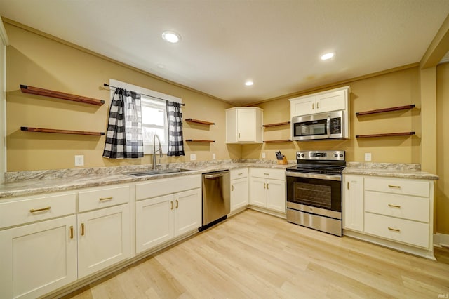 kitchen with sink, light stone counters, light hardwood / wood-style floors, white cabinets, and appliances with stainless steel finishes