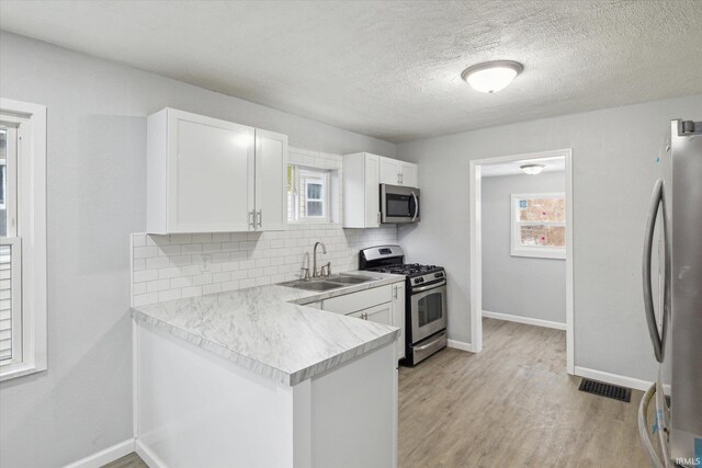 kitchen featuring light wood-type flooring, tasteful backsplash, stainless steel appliances, sink, and white cabinetry