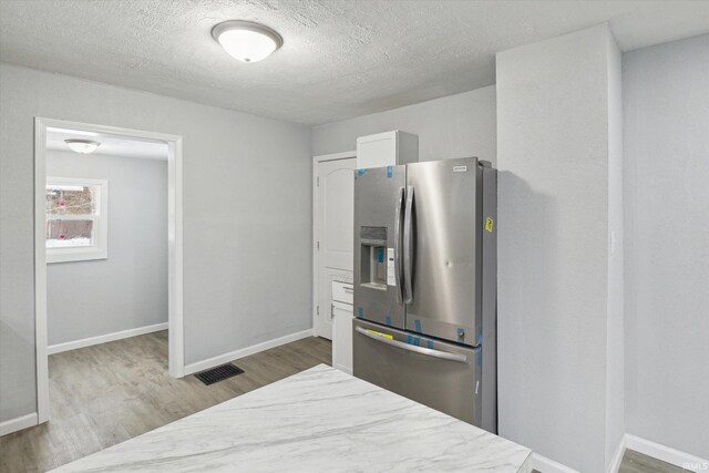 kitchen with a textured ceiling, white cabinetry, stainless steel refrigerator with ice dispenser, and hardwood / wood-style flooring