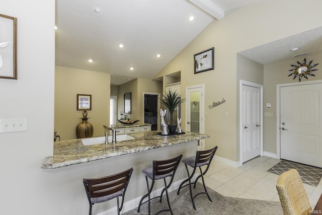 kitchen with kitchen peninsula, light stone countertops, a breakfast bar, vaulted ceiling with beams, and light tile patterned flooring