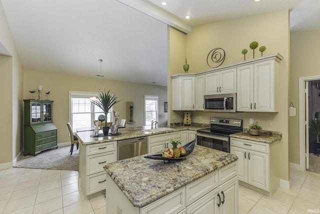 kitchen featuring kitchen peninsula, light stone countertops, stainless steel appliances, sink, and a kitchen island