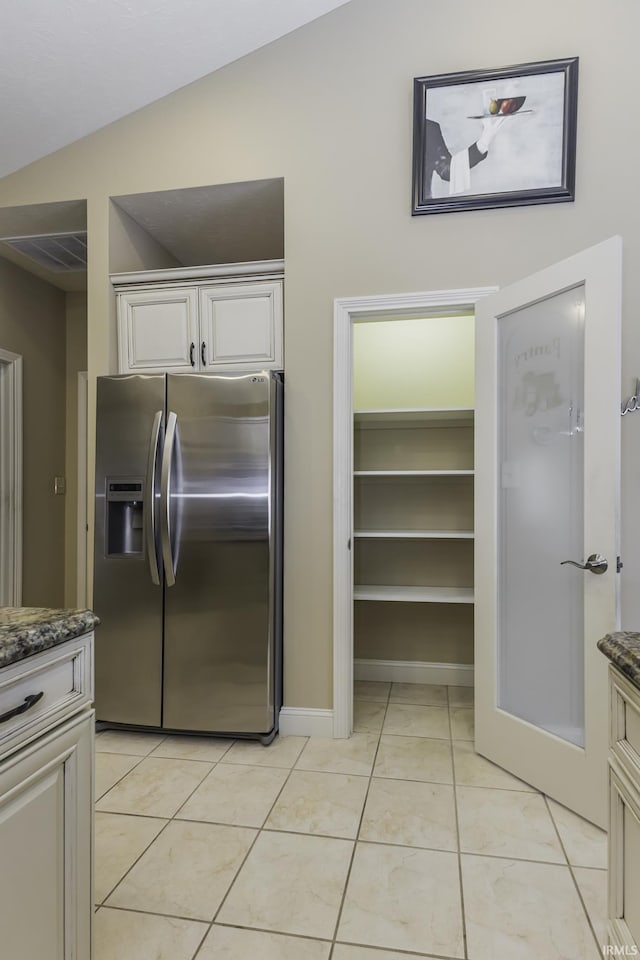 kitchen with stainless steel fridge, vaulted ceiling, light tile patterned floors, and dark stone countertops