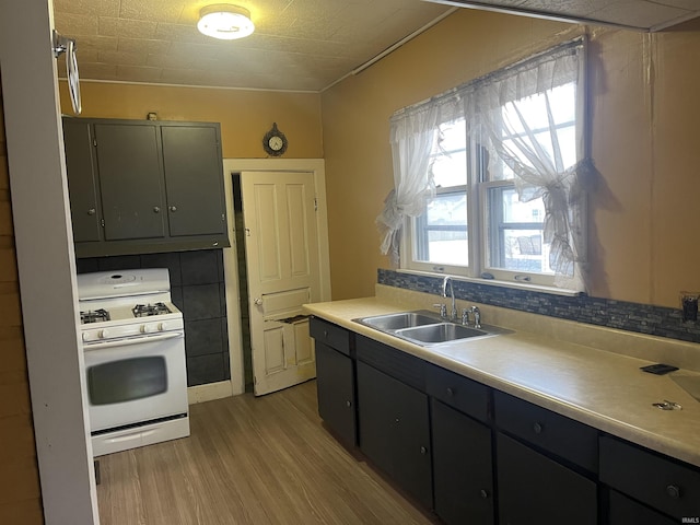 kitchen with backsplash, white gas range, sink, and light hardwood / wood-style flooring