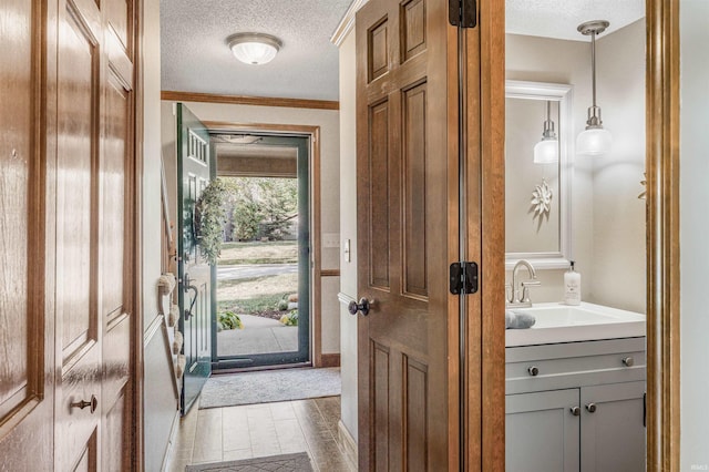 doorway to outside with sink, a textured ceiling, and ornamental molding