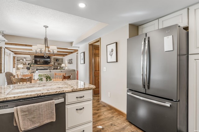 kitchen featuring an inviting chandelier, white cabinets, built in shelves, light stone countertops, and appliances with stainless steel finishes