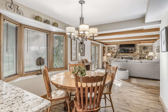 dining room with built in shelves, light wood-type flooring, a fireplace, beamed ceiling, and a chandelier