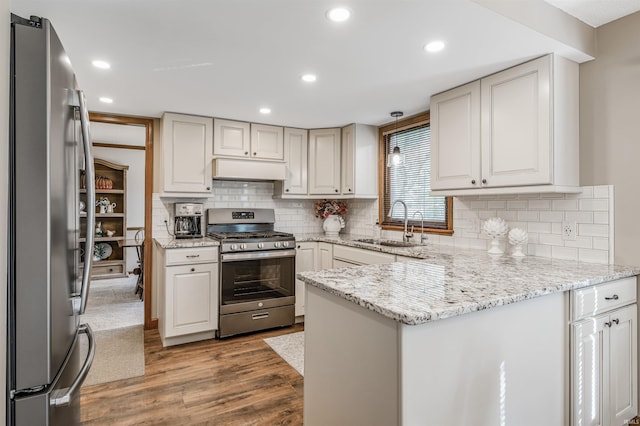 kitchen featuring light stone countertops, sink, stainless steel appliances, tasteful backsplash, and hardwood / wood-style floors