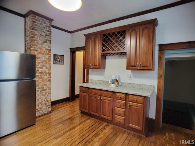 kitchen with light stone countertops, light wood-type flooring, crown molding, and stainless steel refrigerator