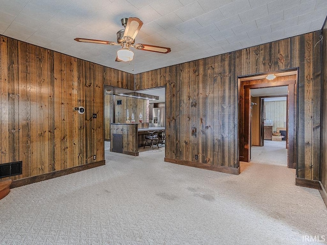 carpeted spare room with ceiling fan and wood walls