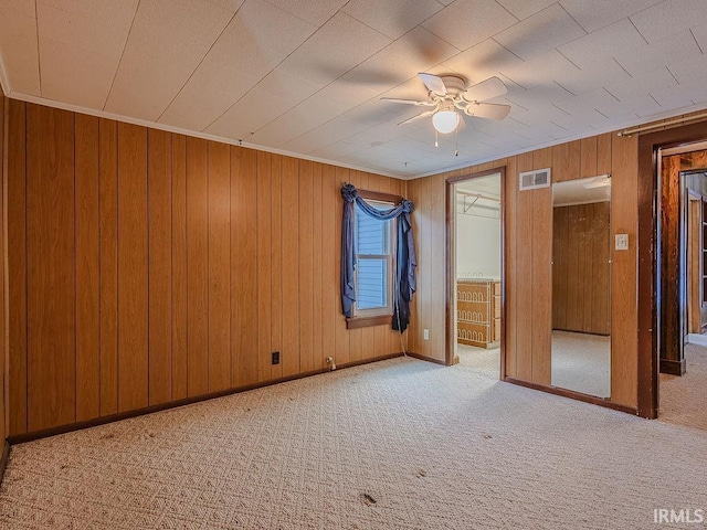 spare room with light colored carpet, ceiling fan, ornamental molding, and wood walls