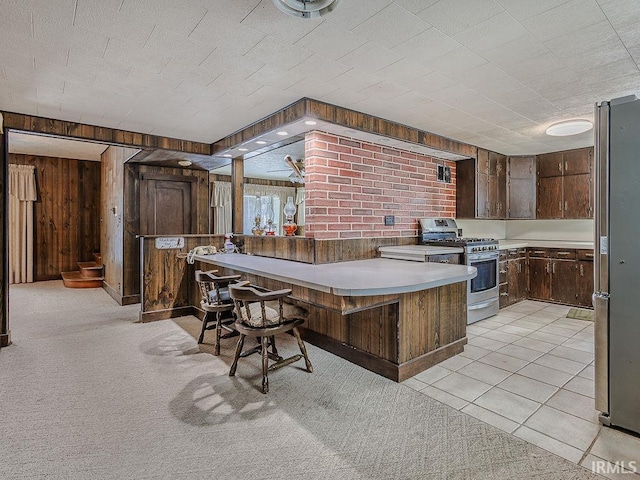 kitchen featuring a kitchen breakfast bar, kitchen peninsula, wooden walls, appliances with stainless steel finishes, and dark brown cabinetry