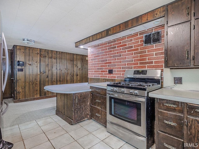 kitchen with gas stove, light colored carpet, dark brown cabinetry, and wood walls