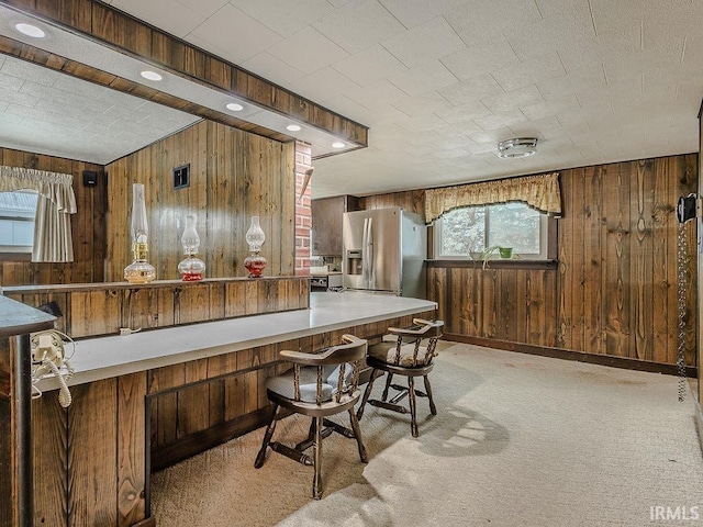 kitchen with stainless steel fridge with ice dispenser, wooden walls, and light carpet