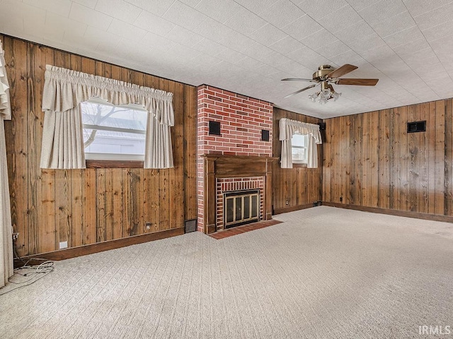 unfurnished living room with wood walls, ceiling fan, a healthy amount of sunlight, and a brick fireplace