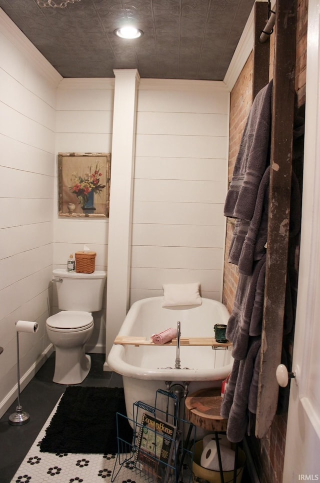 bathroom featuring wood walls, toilet, ornamental molding, and a bath