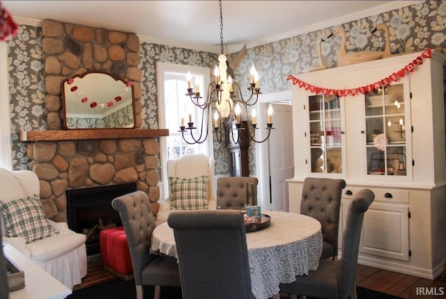 dining area with a stone fireplace, wood-type flooring, ornamental molding, and a chandelier