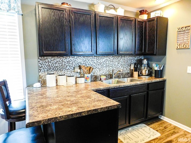 kitchen featuring backsplash, a wealth of natural light, dark brown cabinets, sink, and light hardwood / wood-style flooring