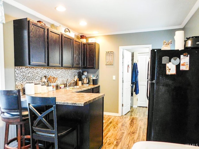 kitchen featuring a kitchen breakfast bar, black fridge, tasteful backsplash, dark brown cabinets, and kitchen peninsula