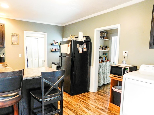 kitchen featuring a kitchen breakfast bar, black fridge, ornamental molding, light hardwood / wood-style flooring, and washer / clothes dryer