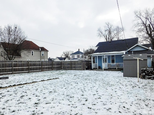 yard layered in snow featuring a porch and a storage shed