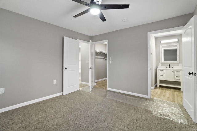 unfurnished bedroom featuring a walk in closet, light colored carpet, ceiling fan, sink, and a closet