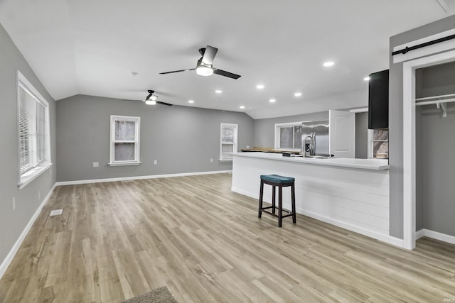 kitchen with ceiling fan, a barn door, light hardwood / wood-style flooring, kitchen peninsula, and lofted ceiling