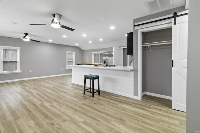 kitchen with ceiling fan, a barn door, light wood-type flooring, stainless steel fridge with ice dispenser, and a breakfast bar area