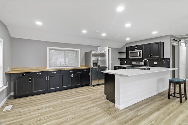 kitchen featuring backsplash, vaulted ceiling, a barn door, appliances with stainless steel finishes, and a kitchen bar