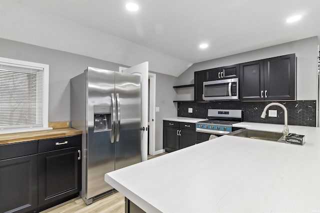 kitchen with appliances with stainless steel finishes, tasteful backsplash, sink, light hardwood / wood-style flooring, and lofted ceiling