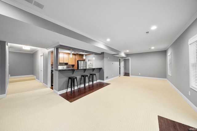 kitchen featuring kitchen peninsula, stainless steel fridge, light carpet, ornamental molding, and a breakfast bar area