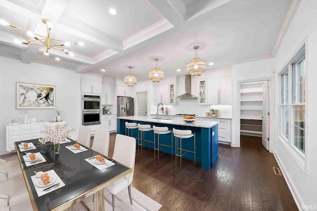 kitchen featuring an island with sink, white cabinetry, wall chimney exhaust hood, and coffered ceiling