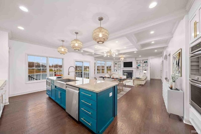 kitchen with stainless steel appliances, sink, pendant lighting, a center island with sink, and beamed ceiling