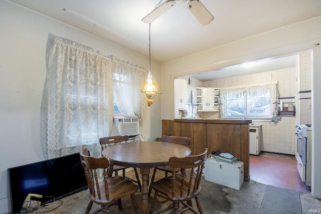 dining space with ceiling fan, cooling unit, and tile walls