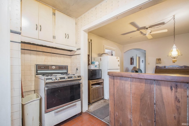 kitchen featuring gas range, ceiling fan, hanging light fixtures, white refrigerator, and backsplash