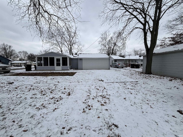 snow covered rear of property featuring a sunroom and a garage