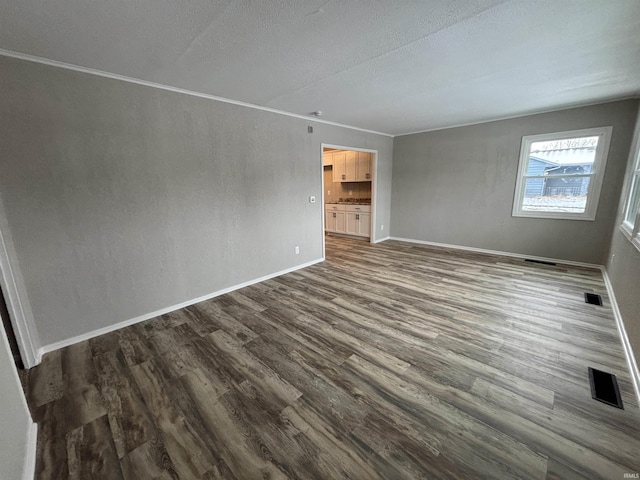 empty room featuring crown molding, dark wood-type flooring, and a textured ceiling