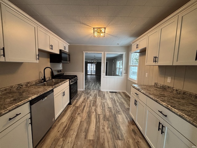 kitchen with dark stone counters, stainless steel appliances, sink, white cabinets, and dark hardwood / wood-style floors