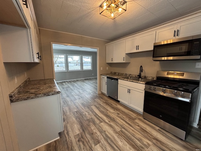 kitchen featuring dark stone counters, stainless steel appliances, sink, wood-type flooring, and white cabinets